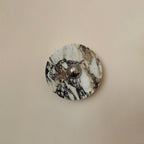 A Clérachic marble wall light in cream stone with black and plum veining and a chrome centre, shown flat on a plain pink-beige wall.