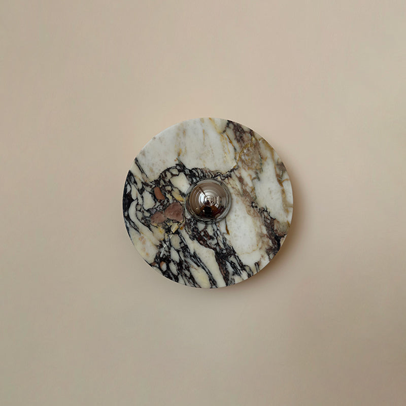 Plum-brown patches and black veining cross the cream stone of this Clérachic marble wall light, shown on a plain pink-beige wall.