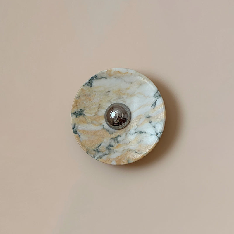 Fine green-grey veins run through the warm gold and white stone of this Clérachic round marble wall light, on a smooth pink-beige wall.