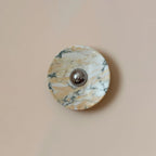 Fine green-grey veins run through the warm gold and white stone of this Clérachic round marble wall light, on a smooth pink-beige wall.