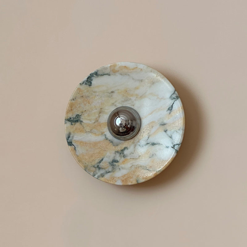The Clérachic marble wall light with golden bands and teal-green veining on white, shown against a pink-beige wall.