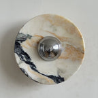 Close view of the Clérachic marble disc in cream, gold and black, from the front, with a polished chrome dome at the centre.