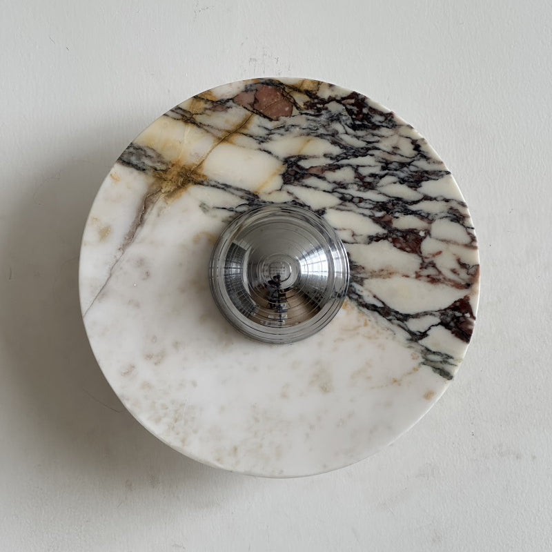 A Clérachic marble wall light with golden-brown and plum veins across cream stone, its chrome dome catching the light.