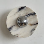 A Clérachic marble wall light in cream stone with sharp black veins running from the upper right into the chrome dome.