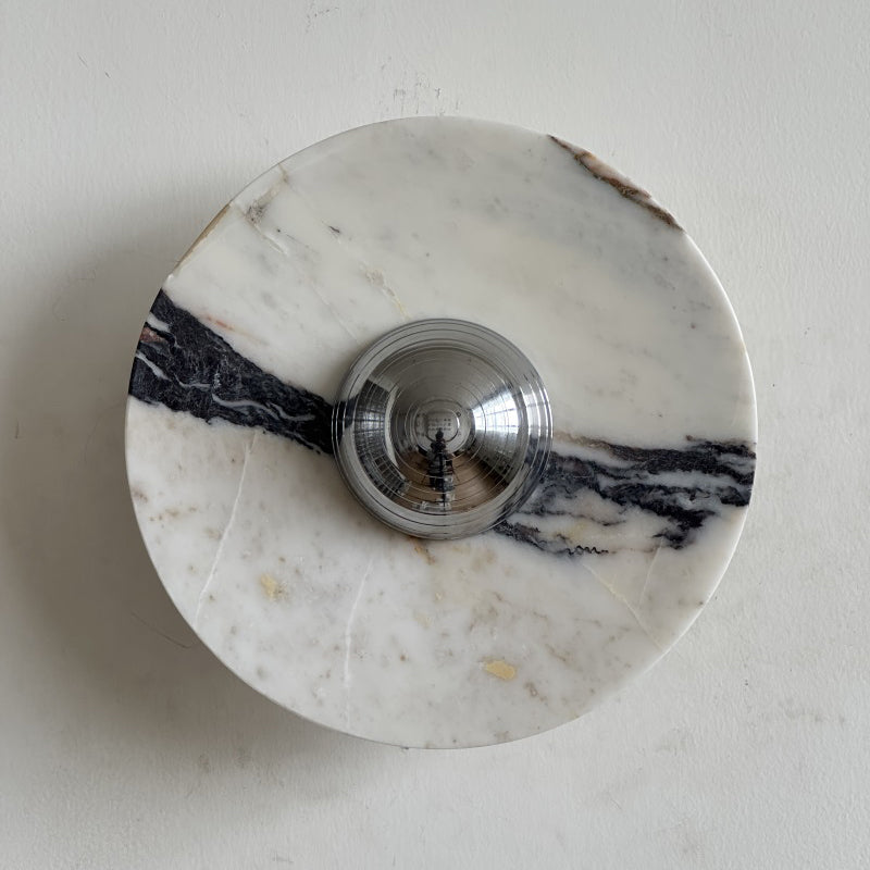 A Clérachic marble wall light with a dark wedge of black and grey veining on the left and pale cream stone around its chrome dome.