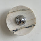 A Clérachic marble wall light in white stone with a few long grey veins and soft gold hints, around its chrome dome.