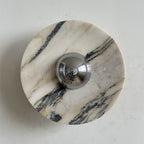 A Clérachic marble wall light with bold black veins across the left and lower edge of a creamy white disc, around a chrome dome.