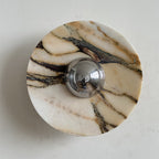 A Clérachic marble wall light in warm cream stone with thick gold and dark brown ribbons crossing its face, around a chrome dome.