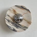 A Clérachic marble wall light in cream stone with russet veins and long black streaks running from top left to bottom right.