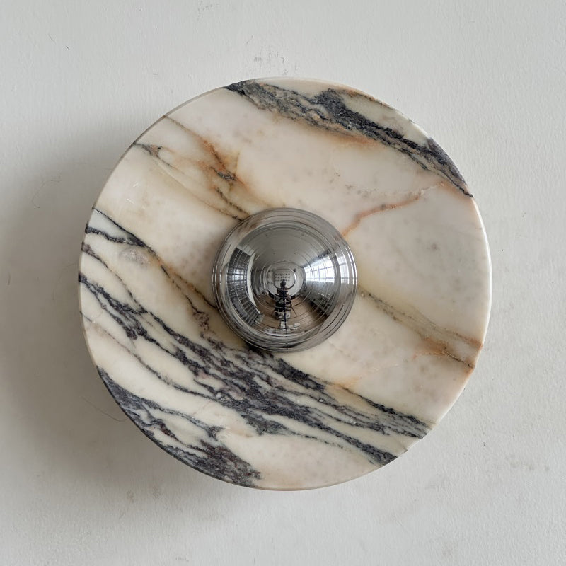 A Clérachic marble wall light in cream stone with russet veins and long black streaks running from top left to bottom right.