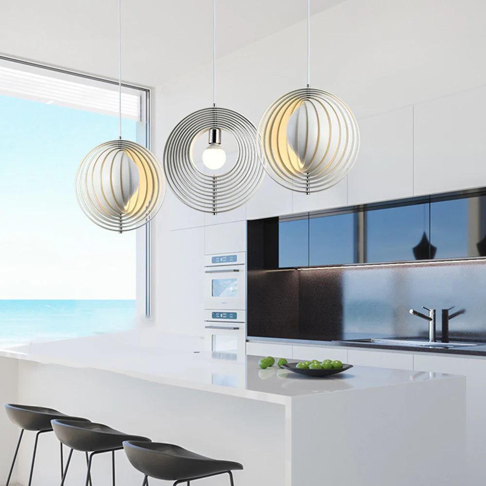 Three Clérachic Round Metal Pendant Lights in chrome hang over a marble kitchen island with black stools.