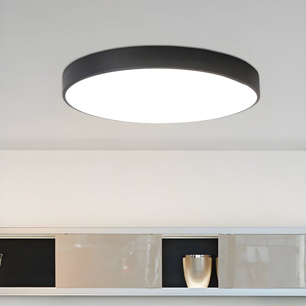 Lit black round Clérachic ceiling light with a flat white diffuser, above a shelf holding a vase.