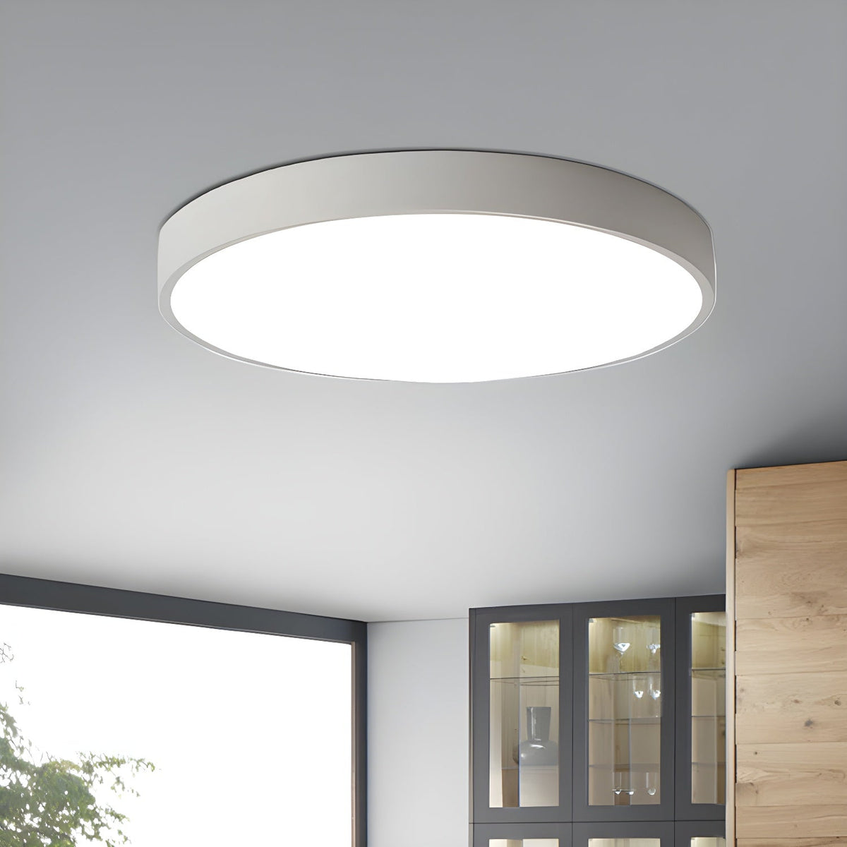 White round Clérachic ceiling light lit on a grey ceiling, with a window and a glass-fronted cabinet below.