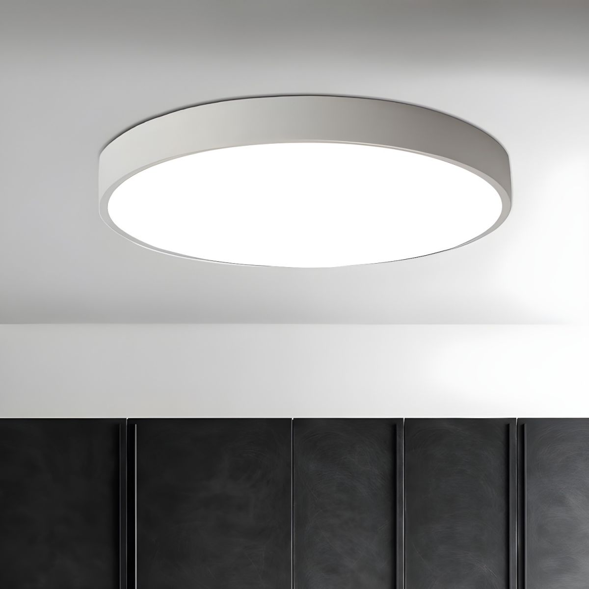 A white-framed round Clérachic ceiling light lit above a wall of dark panelled cupboard doors.