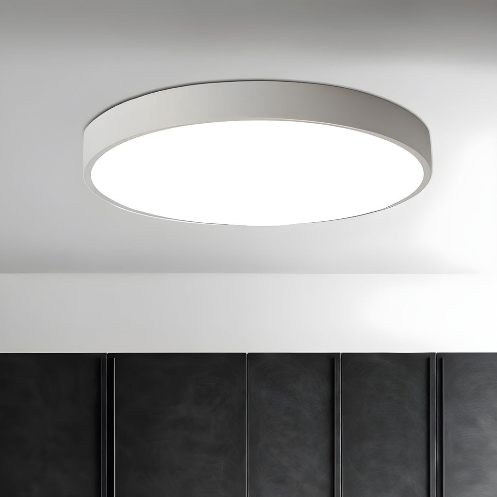 White round Clérachic ceiling light, lit, on a pale ceiling above a dark quilted wall panel.
