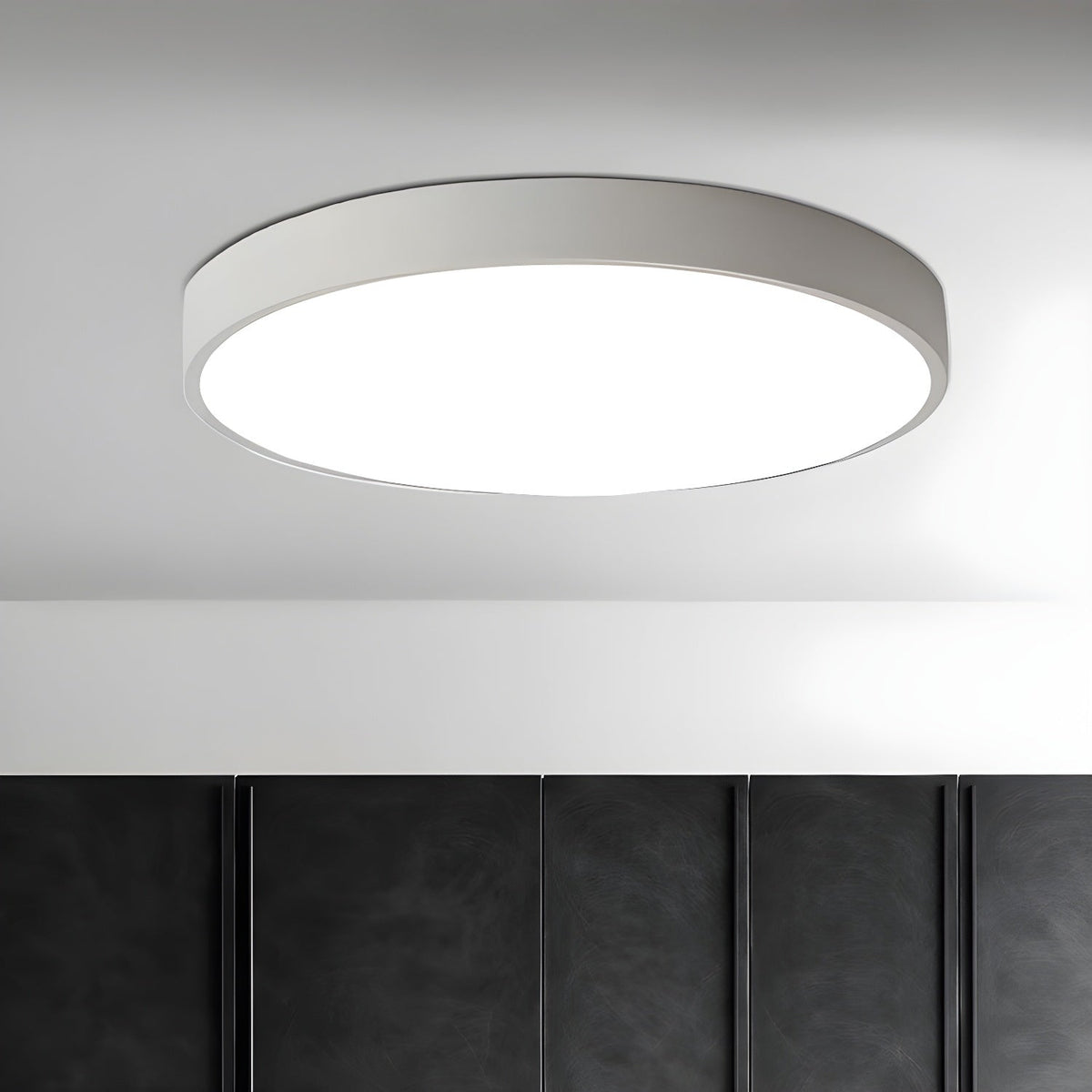 White round Clérachic ceiling light, lit, on a pale ceiling above a dark quilted wall panel.