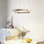 Travertine ring pendant from Clérachic, lit, hanging above a round table with a flowering branch and a yellow bowl, near an arched white cabinet.