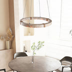 Seen from below, a Clérachic travertine ring pendant hangs in a bright room above a round grey table with a green branch in a vase.