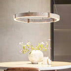 Close view of the travertine ring and warm LED edge of this Clérachic pendant, above a table with a textured vase and pink blossom.