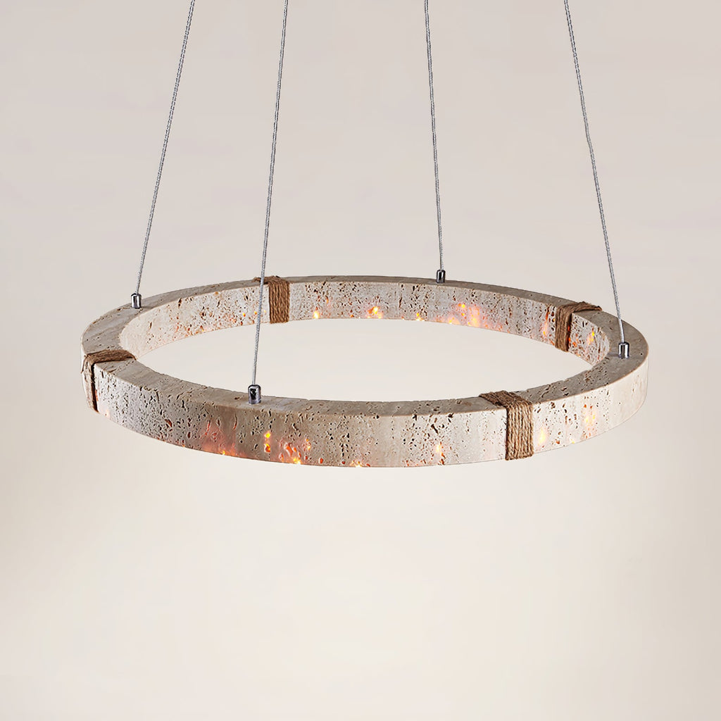 Wide view of the lit travertine ring from Clérachic, showing its pitted stone surface and rope-wrapped joints, on soft cream.