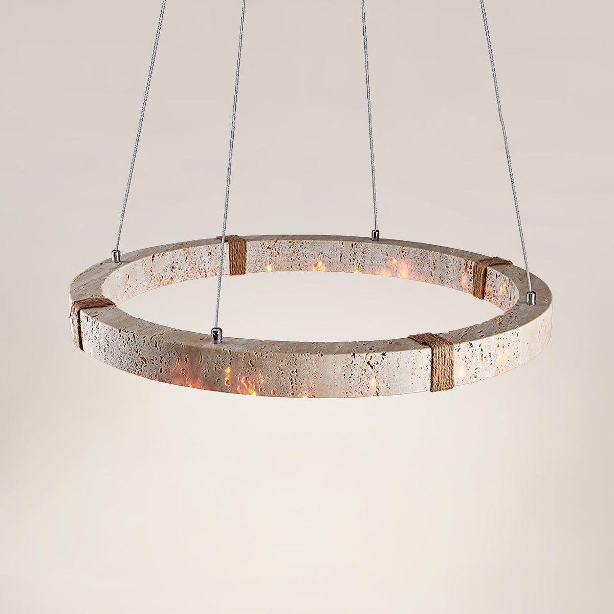 Wide view of the lit travertine ring from Clérachic, showing its pitted stone surface and rope-wrapped joints, on soft cream.