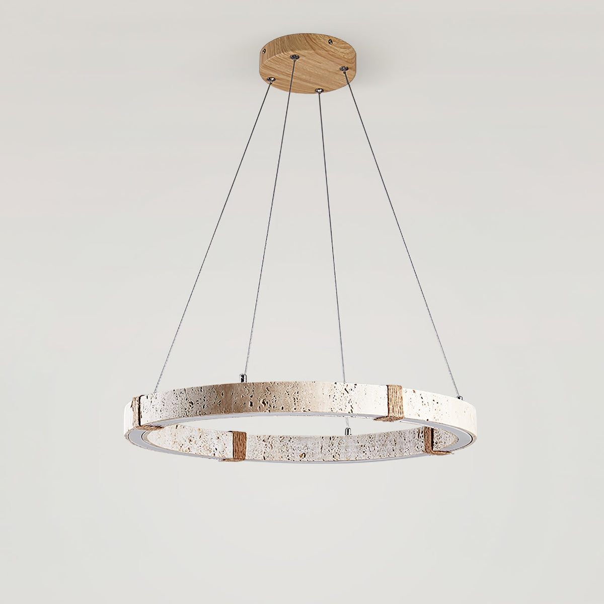 A Clérachic travertine ring pendant on a wooden ceiling plate, with three fine suspension cables, against a pale grey wall.