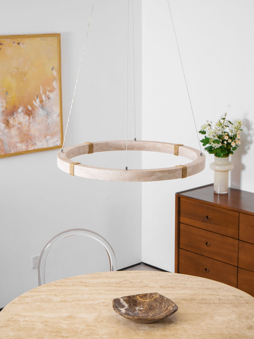 Clérachic travertine ring pendant hung in front of an abstract painting, above a stone-topped table with a dark bowl and a chest of drawers.