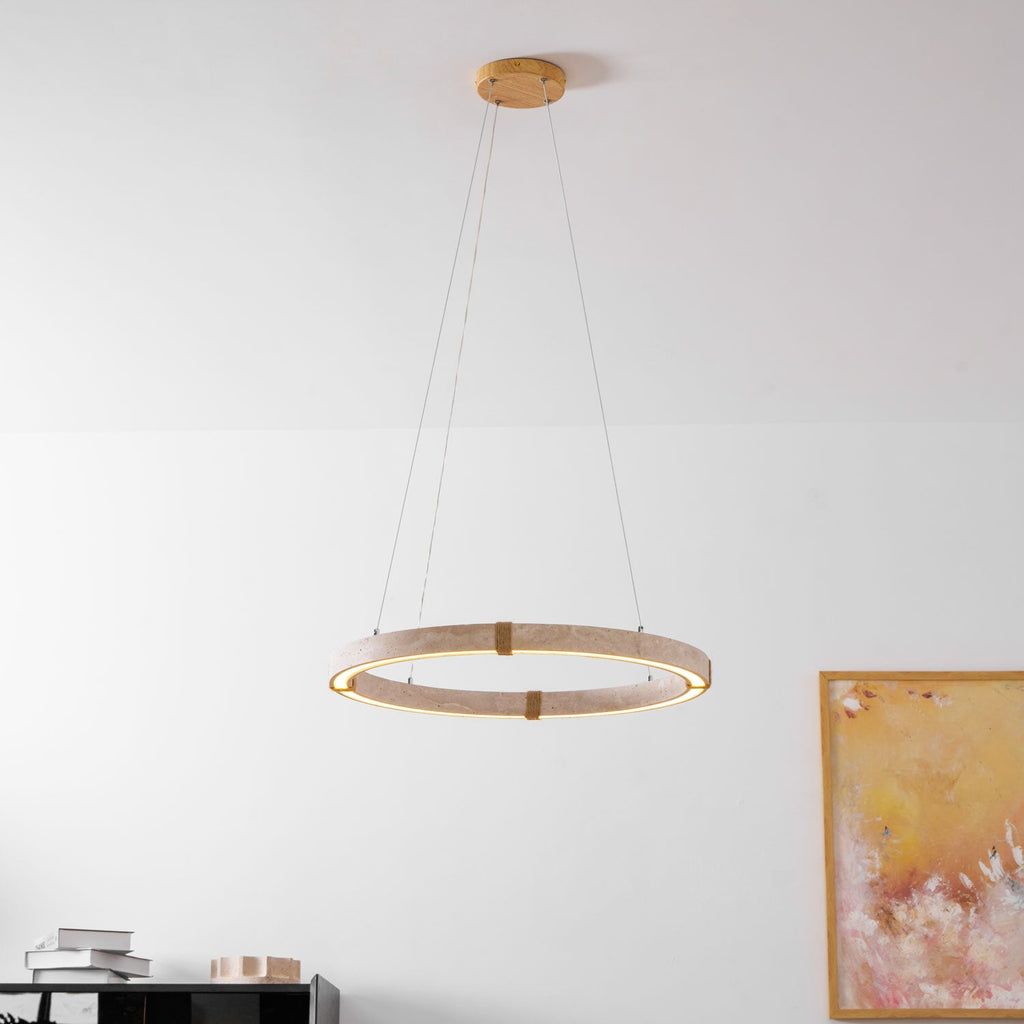 A lit Clérachic travertine ring pendant hangs on three cables from a gold ceiling plate beside a framed abstract painting.