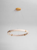 A paler, pinker travertine ring pendant from Clérachic on a gold ceiling plate and fine cables, against a pale grey wall.