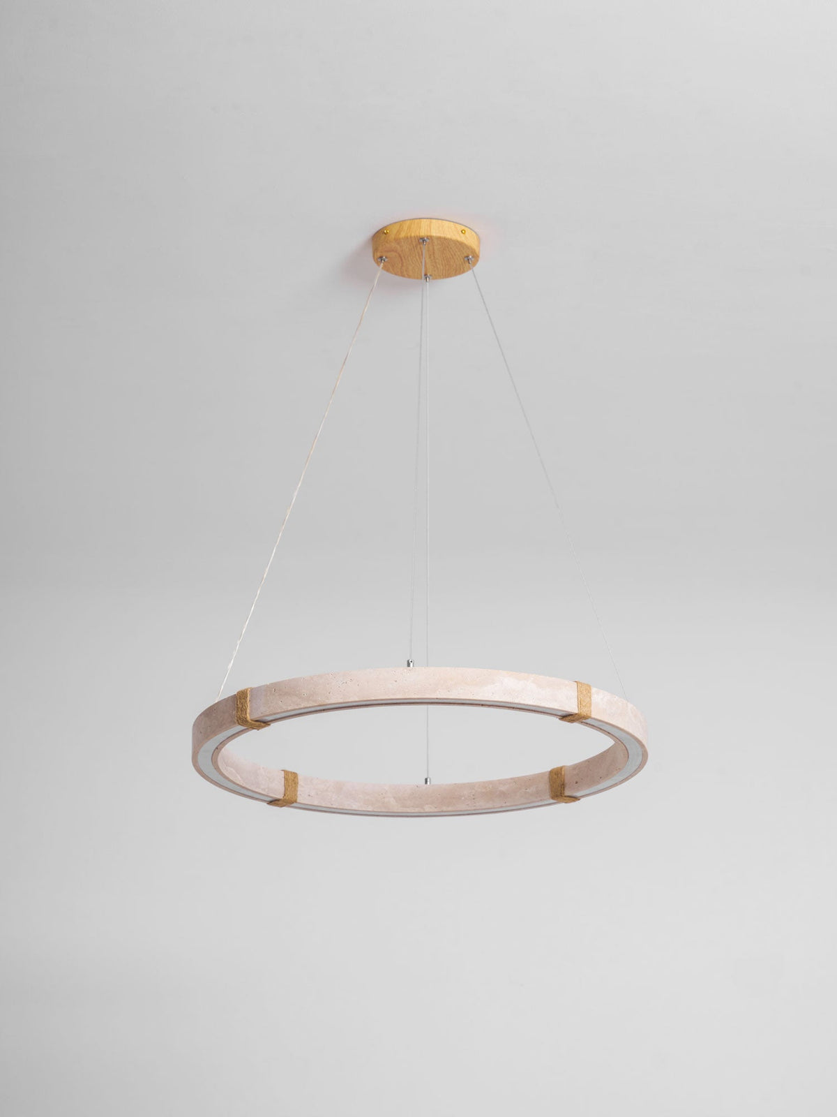 Travertine ring pendant from Clérachic in a pale pink-beige stone, unlit, hung from a gold ceiling plate against a pale grey wall.