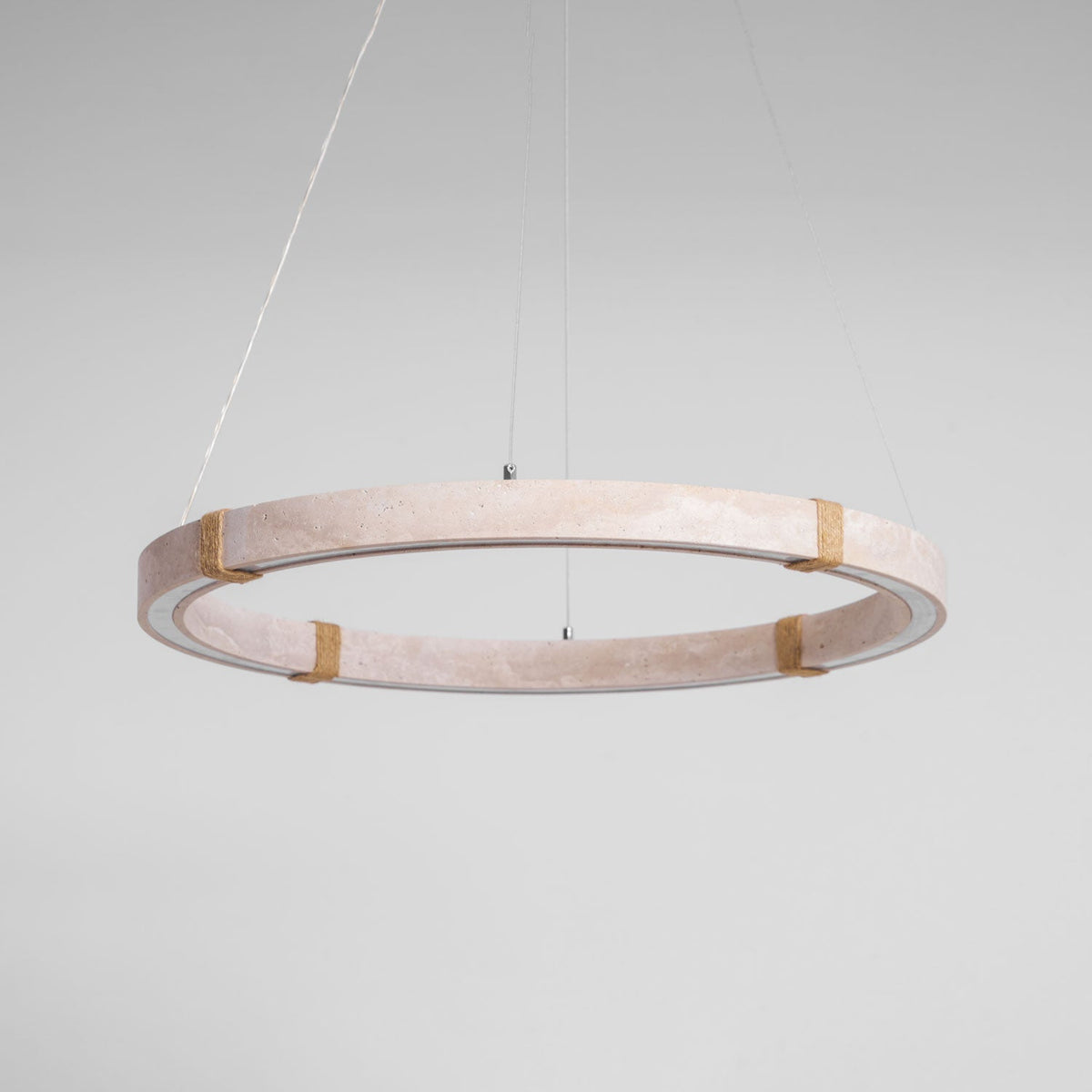 Low view of a pale pink-beige travertine ring from Clérachic with four rope-wrapped joints and its inner edge unlit.