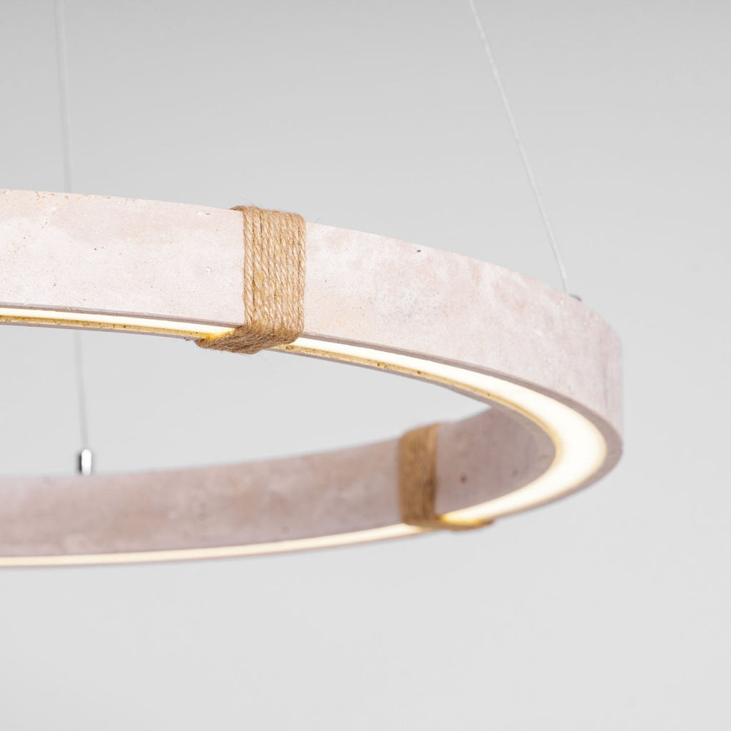 Close view of the rope-wrapped joint and warm LED edge on this Clérachic travertine ring pendant, against a pale grey wall.