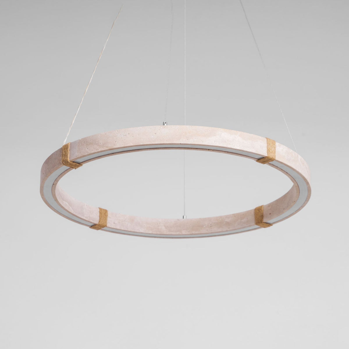 Tilted view of a Clérachic travertine ring pendant in pale pink-beige stone, with four rope-wrapped joints and a pale inner edge.