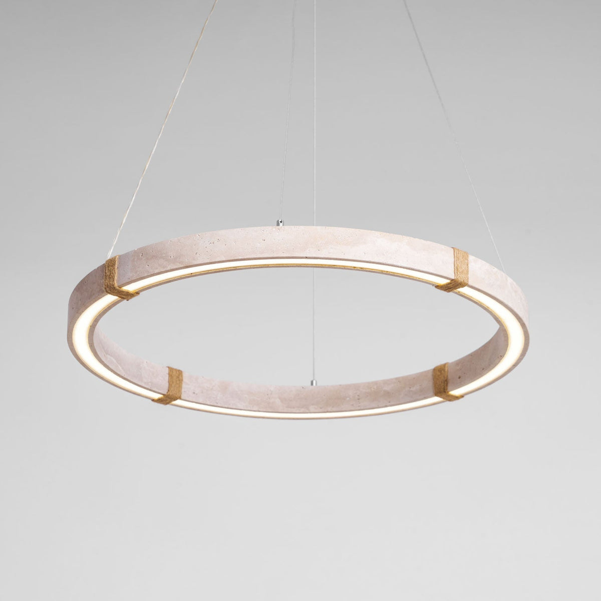 The pale travertine Clérachic ring pendant lit, with a warm glow along the inner edge and four rope-wrapped joints.