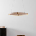 Lit travertine ring pendant from Clérachic hung low in a white room, with a black cabinet and a dark bowl on a table below.
