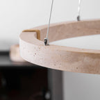 Close view of the pitted travertine edge and the steel cable fixing on this Clérachic ring pendant, with a dark cabinet blurred behind.