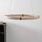The Clérachic travertine ring pendant hangs by thin cables against a white wall, with a black cabinet edge to one side.