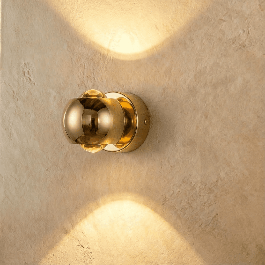 Clérachic round gold wall sconce, 10 cm across, sending warm light up and down a limewashed wall