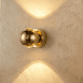Clérachic round gold wall sconce, 10 cm across, sending warm light up and down a limewashed wall