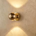 Clérachic round gold wall sconce, 10 cm across, sending warm light up and down a limewashed wall