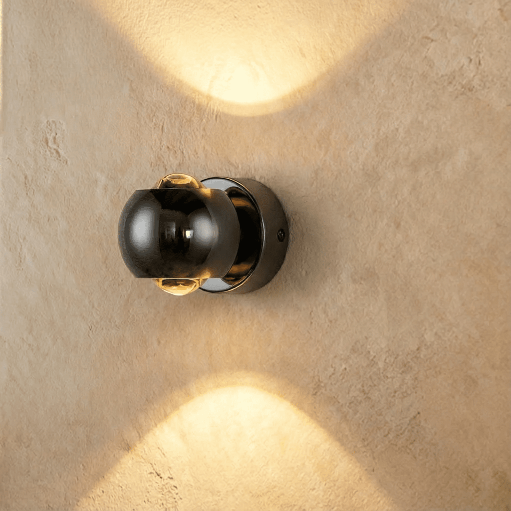 Clérachic round wall sconce in a glossy dark gunmetal finish, casting warm light up and down a plaster wall