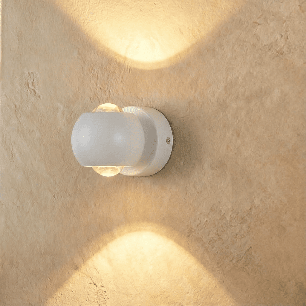 Clérachic round white wall sconce with clear lenses top and bottom, washing a plaster wall with warm light