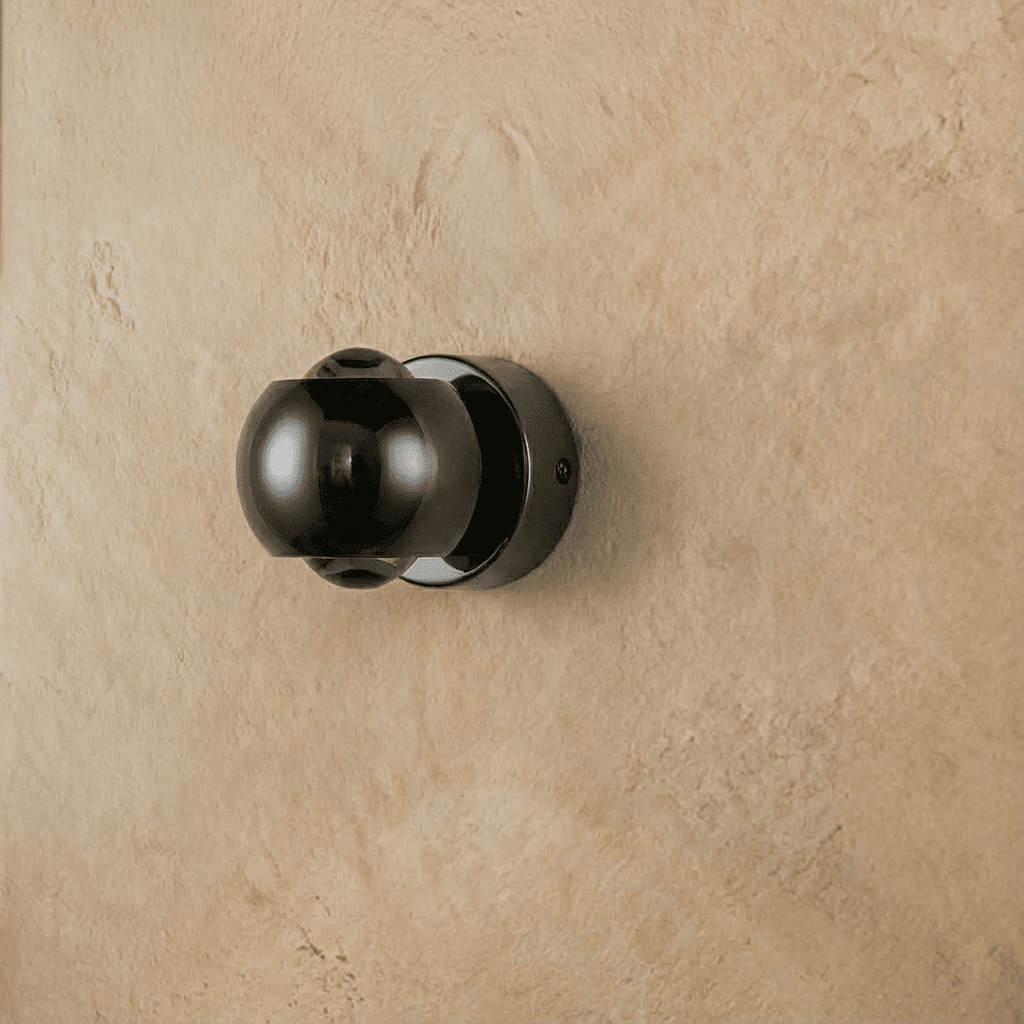 Clérachic round wall sconce in glossy dark gunmetal, switched off, fixed to a textured plaster wall