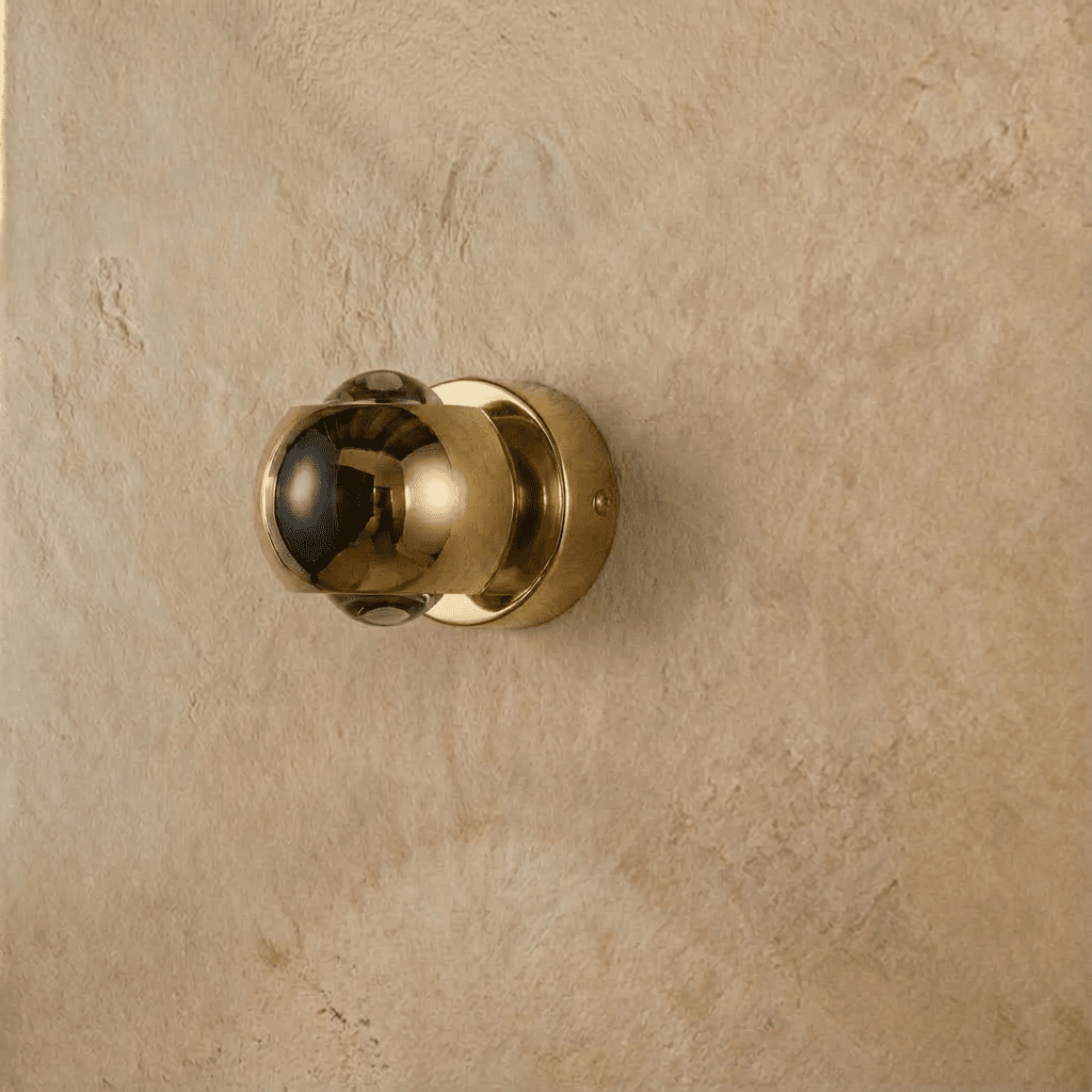 Clérachic round gold wall sconce with a polished domed shade and clear lenses, switched off, on a plaster wall