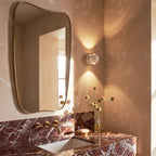 Clérachic white round wall sconce beside a gold-framed mirror above a marble counter, with a vase of dried flowers