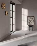 Clérachic round alabaster sconces on a plaster wall in a sunlit hall with a black window.