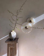 Two Clérachic round alabaster sconces overlapping on a pale wall behind a stoneware vase.