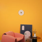A single Clérachic round alabaster sconce on a bright yellow wall above a coral armchair.
