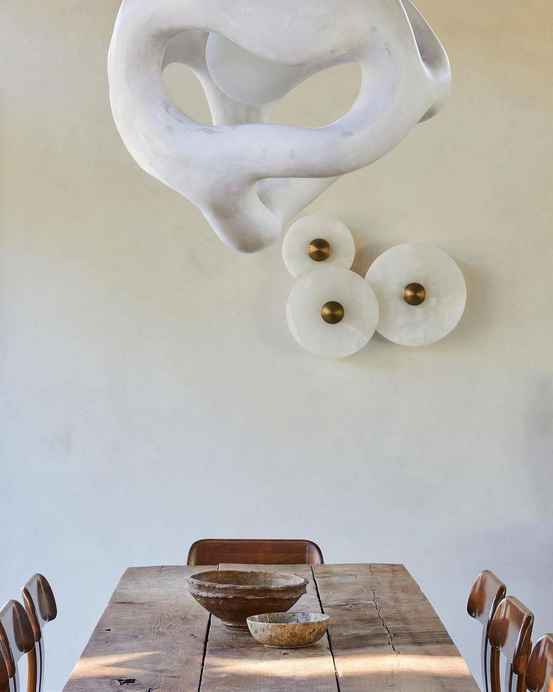 Three Clérachic round alabaster discs mounted beneath a sculptural plaster wall piece.
