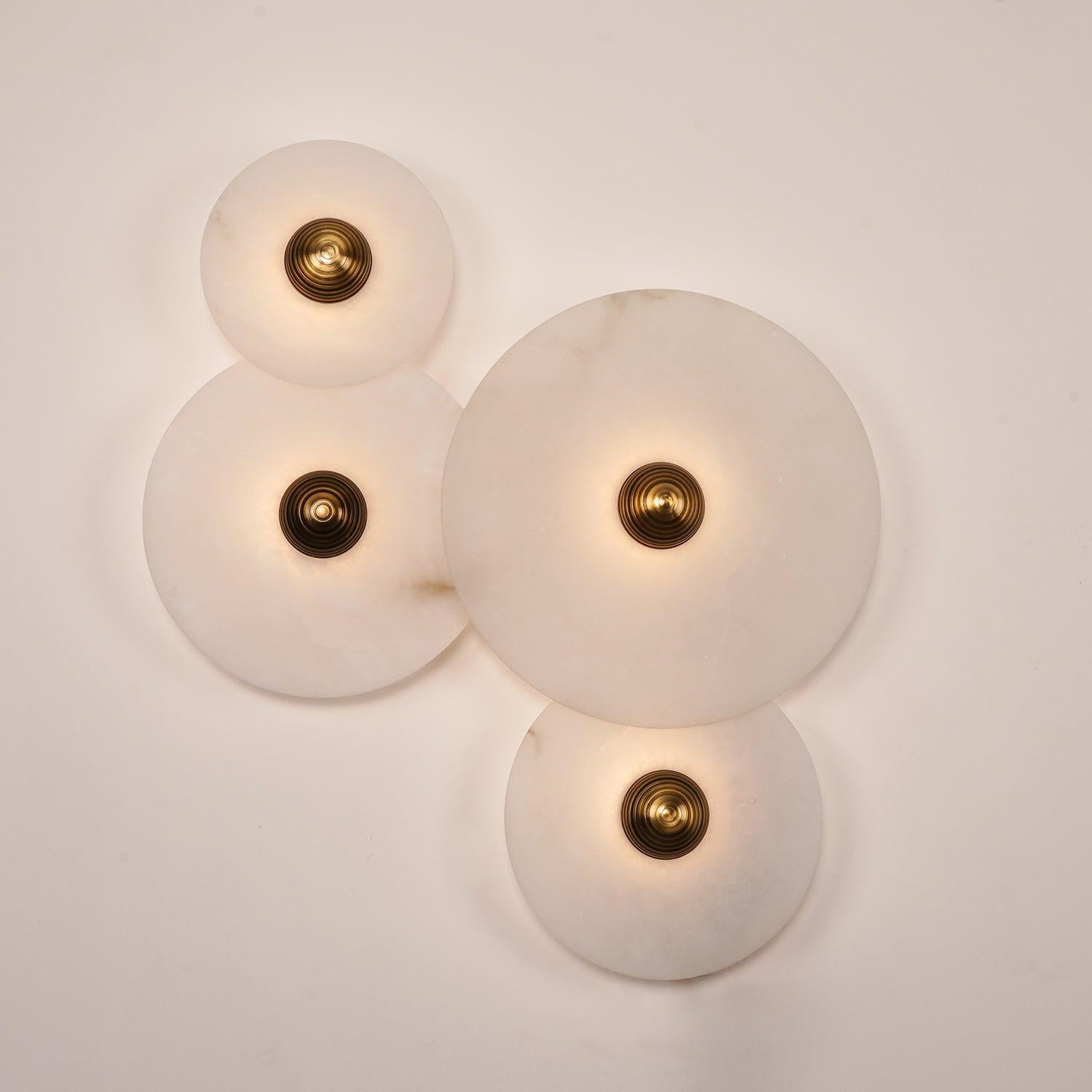 Four Clérachic round alabaster sconces lit close, veined stone glowing around brass centres.